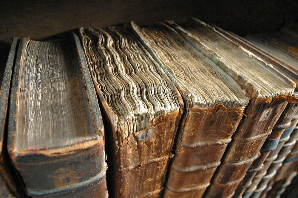 Four antique leather-bound volumes seen from above, showing worn brown spines and the layered edges of their text blocks