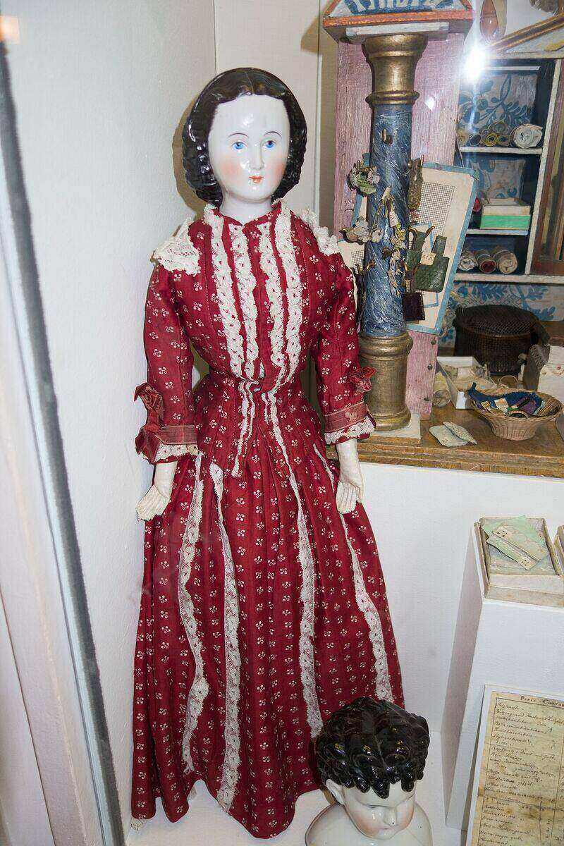 Glazed china-head doll with moulded black hair and a red lace-trimmed dress, standing beside a spare china doll head