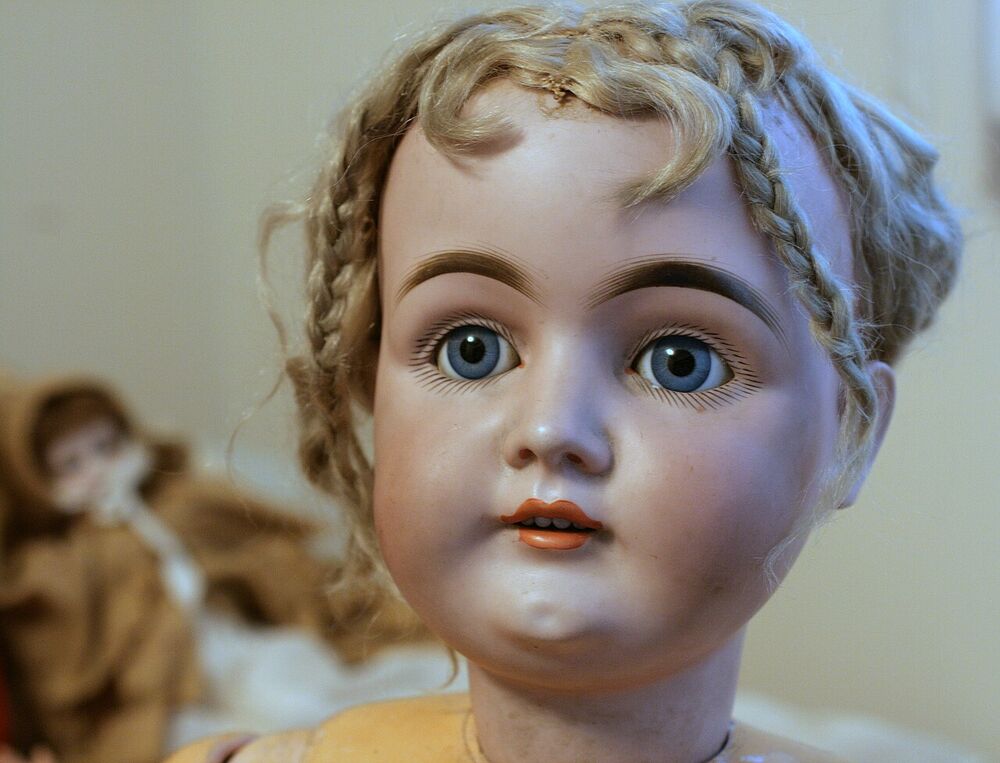 Close-up of a German bisque doll head with blue glass eyes, painted brows, blonde mohair braids and a visible neck rim